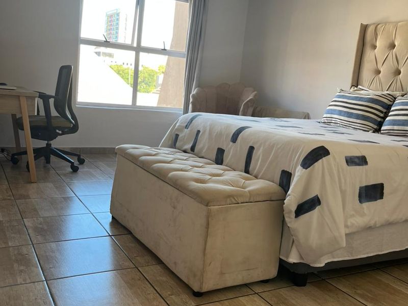 A well-lit bedroom featuring tiled flooring and a large window, providing a comfortable and functional living space.