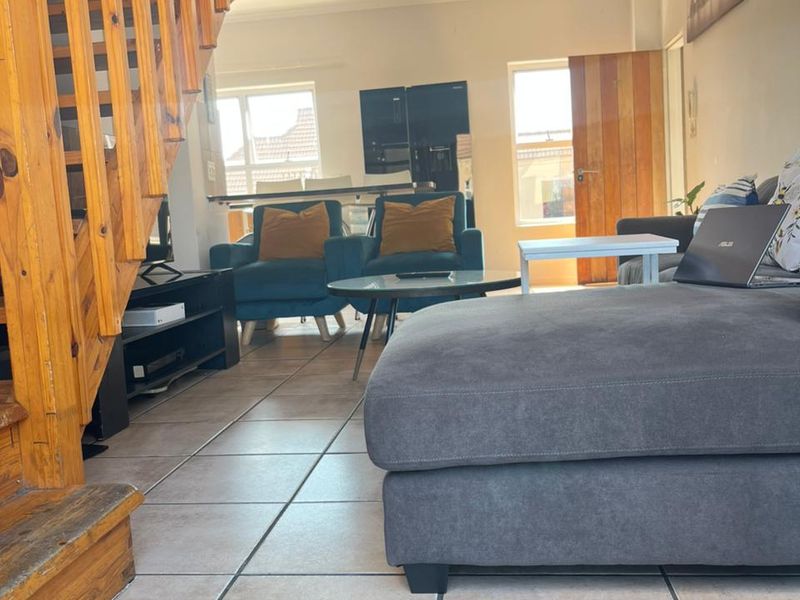 Open plan living area featuring tiled flooring and a prominent wooden staircase leading to the upper level, with an integrated kitchen space beyond.