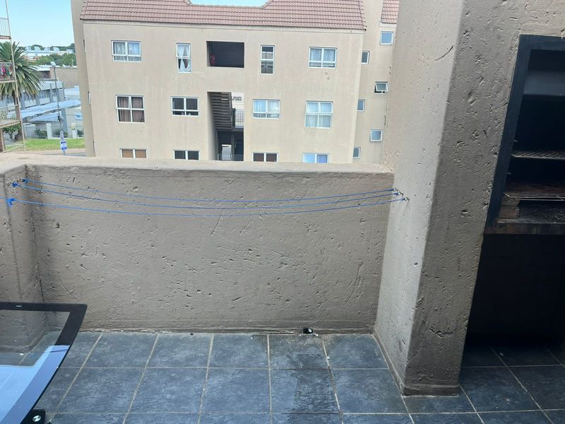 A balcony featuring a built-in braai, tiled flooring, and a parapet wall, offering an outdoor space for relaxation and entertaining.