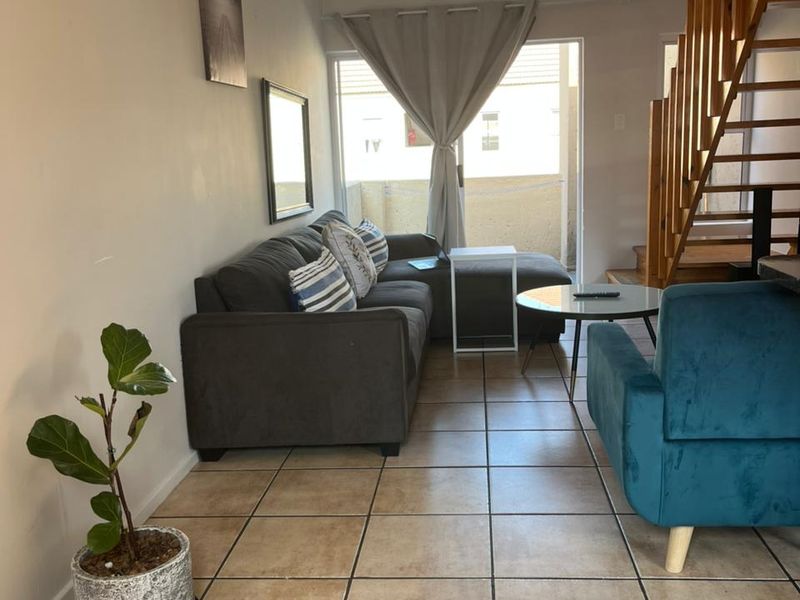 A living room featuring tiled flooring and a wooden staircase leading to an upper level, with direct access to an outdoor patio area.