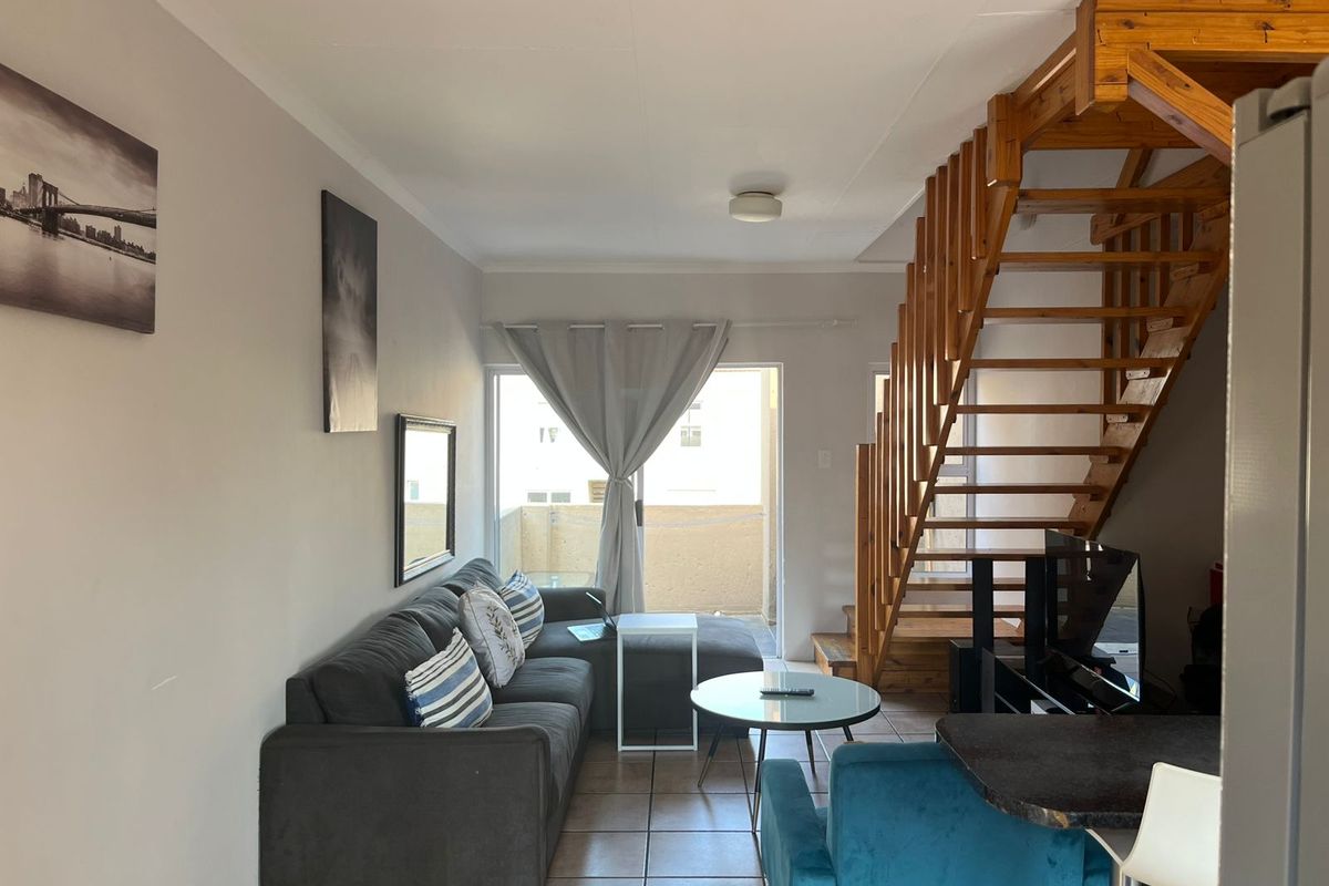 Open-plan living area featuring tiled flooring and a prominent timber staircase leading to the upper level, with access to a balcony.