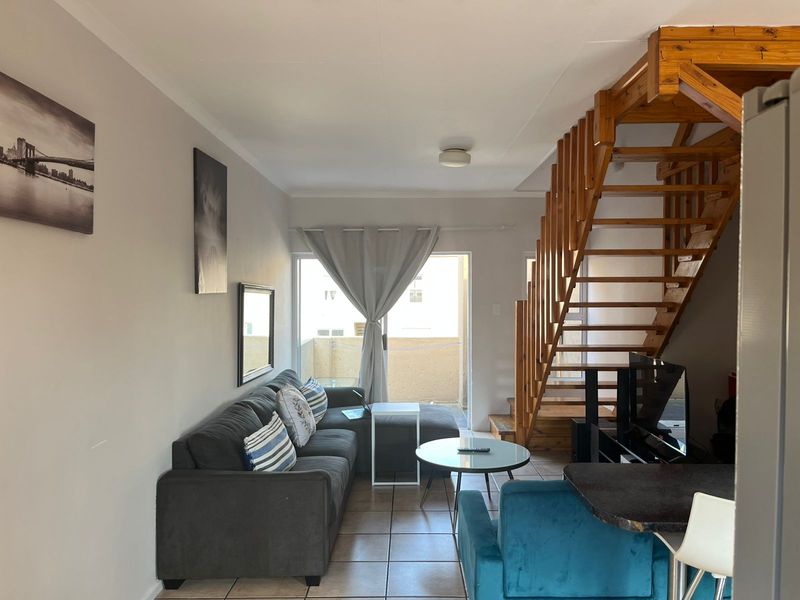 Open-plan living area featuring tiled flooring and a prominent timber staircase leading to the upper level, with access to a balcony.