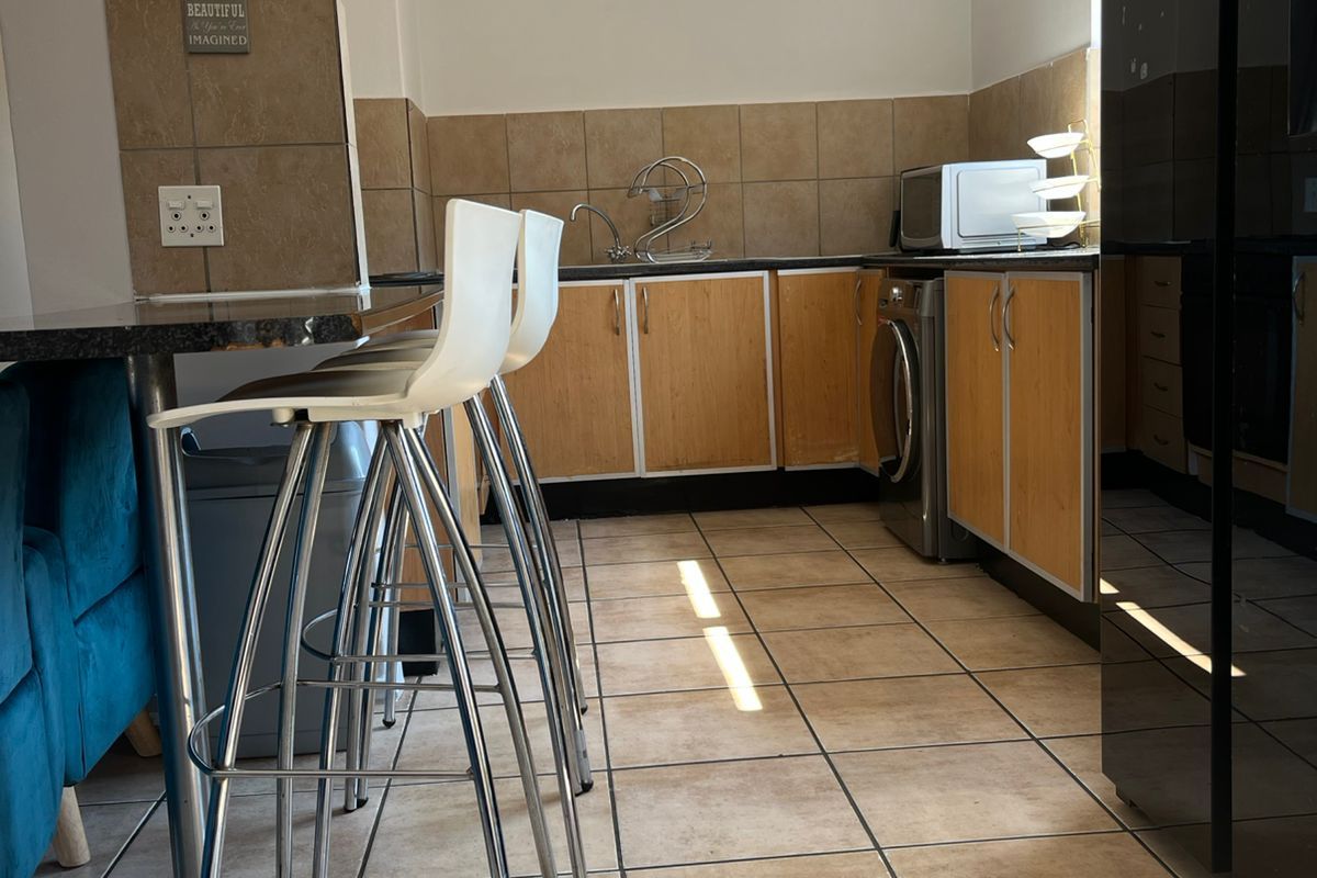 Functional kitchen featuring wood-finish cabinetry, granite countertops, tiled backsplash, and ceramic flooring with integrated laundry plumbing.