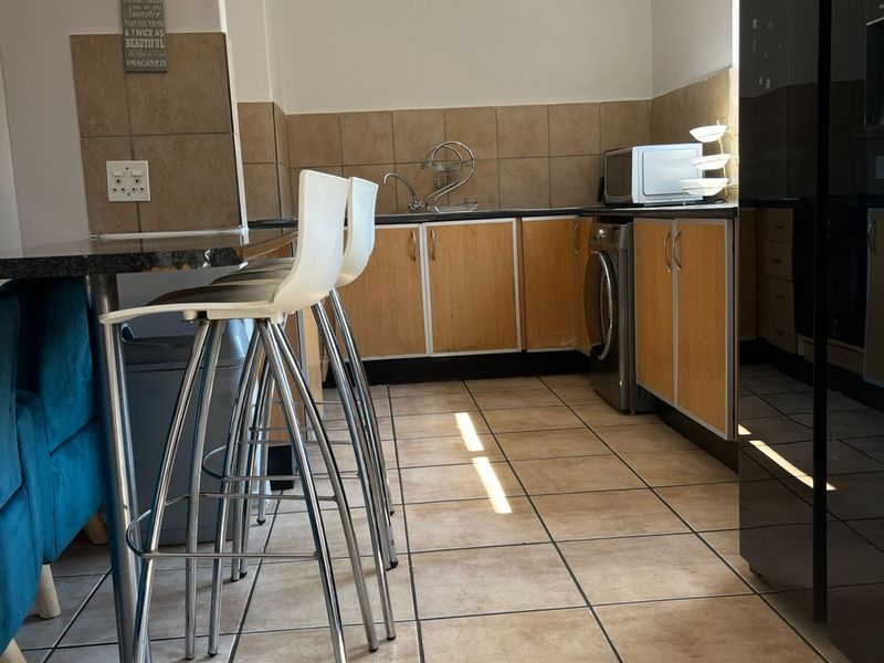 Functional kitchen featuring wood-finish cabinetry, granite countertops, tiled backsplash, and ceramic flooring with integrated laundry plumbing.