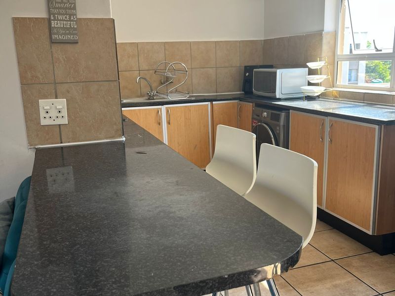 Functional kitchen featuring granite countertops, a breakfast bar, tiled backsplash, and built-in cabinetry with space for laundry appliances.