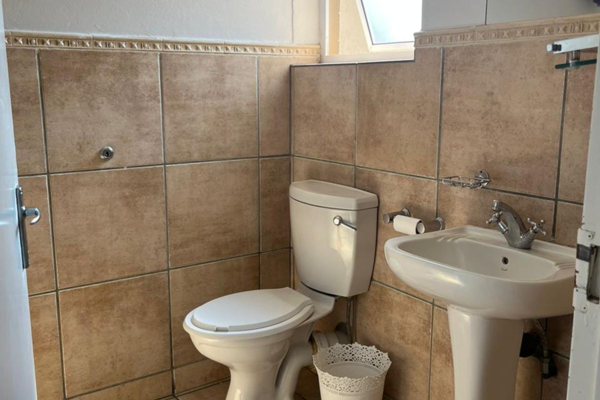 A functional bathroom featuring a pedestal basin, toilet, and neutral wall and floor tiling with a top-hung window for natural light.