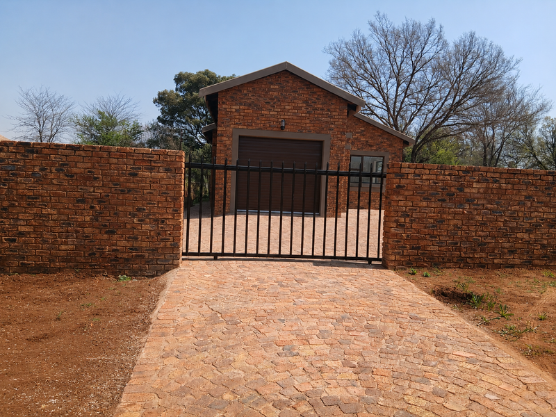Front view of a face brick garage with a paved driveway, secure metal sliding gate, and matching face brick boundary walls.