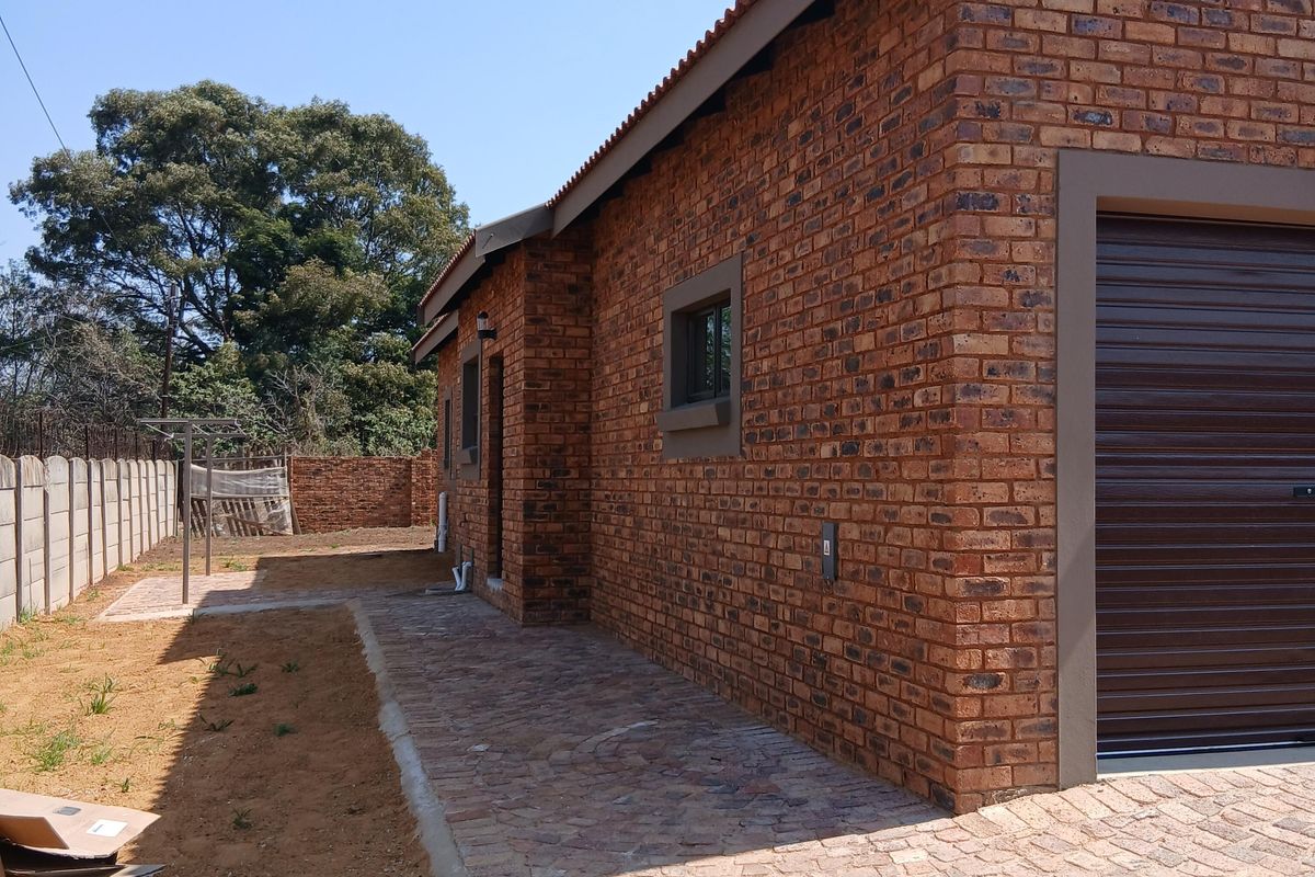 Side and rear view of a face brick house featuring a roller garage door, paved walkway, and a precast concrete boundary wall.