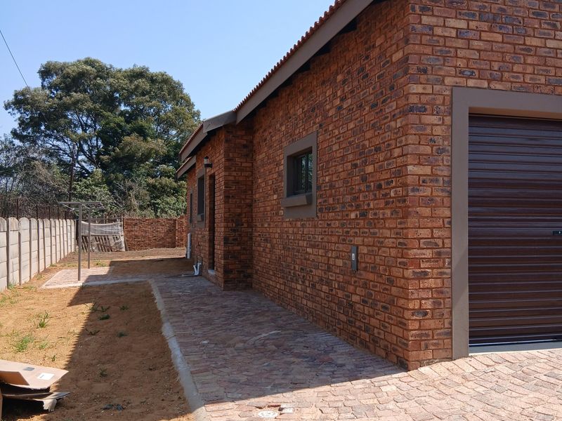 Side and rear view of a face brick house featuring a roller garage door, paved walkway, and a precast concrete boundary wall.