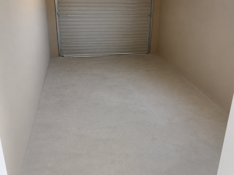 A clean, empty single garage space featuring a roller door, smooth concrete flooring, and a small side window.
