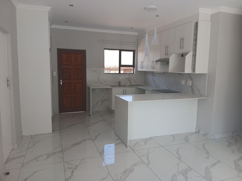 Modern kitchen featuring white cabinetry, quartz countertops, marble-look tiled flooring, and integrated appliances, offering a clean and contemporary aesthetic.