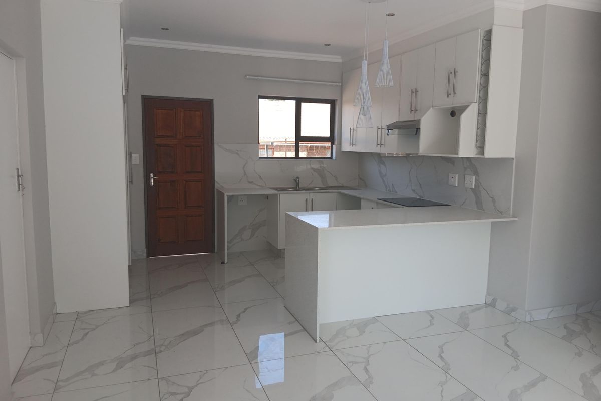 Modern kitchen featuring white cabinetry, quartz countertops, marble-look tiled flooring, and integrated appliances, offering a clean and contemporary aesthetic.