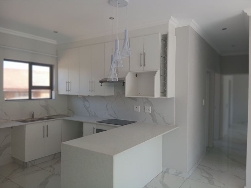 Modern kitchen featuring white cabinetry, marble-look quartz countertops, built-in hob, extractor fan, and sleek porcelain floor tiles in an open-plan layout.