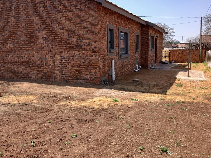 Rear view of a face brick house featuring a simple paved walkway and an unlandscaped garden area.