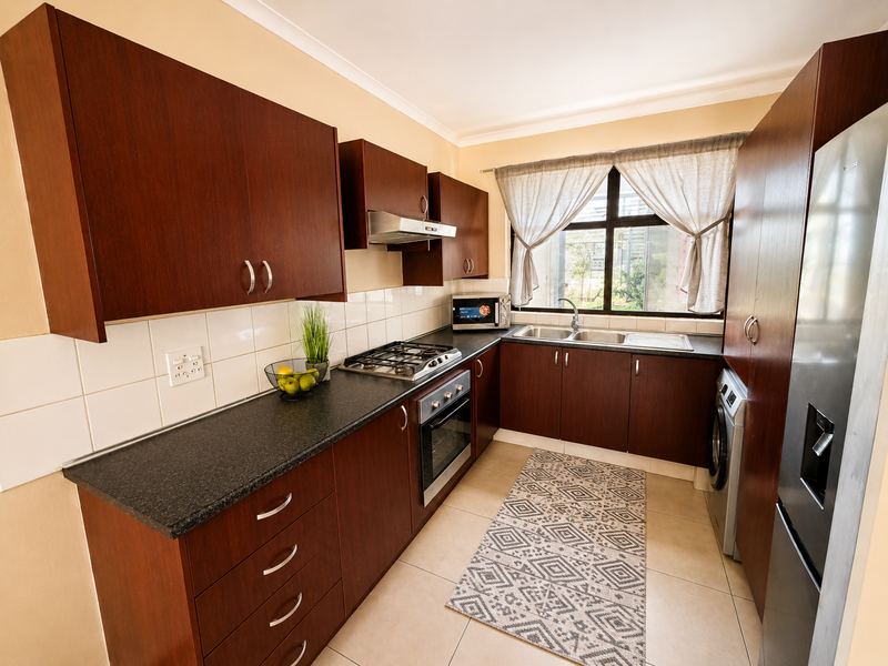 A functional kitchen featuring dark wood cabinetry, laminate countertops, a gas hob, built-in oven, and a double bowl sink with tiled backsplash.