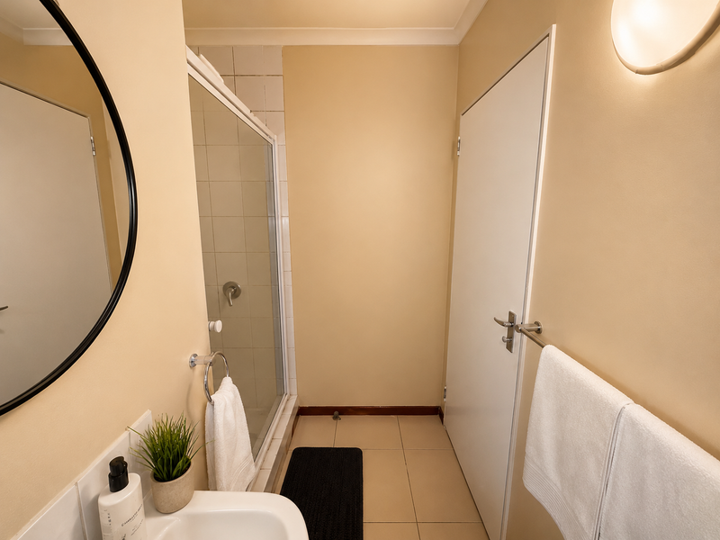 A clean and functional bathroom featuring a glass-enclosed shower, tiled flooring, and a wall-mounted vanity basin with a circular mirror.