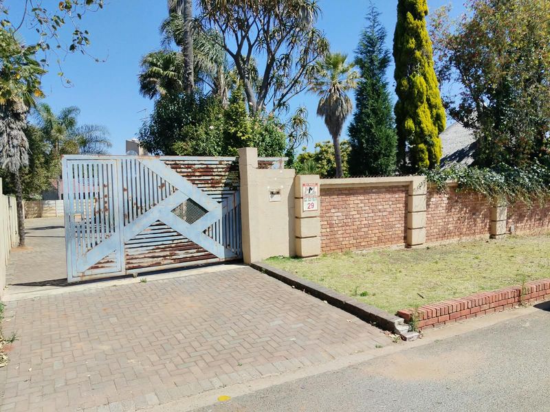 Front view of the property featuring a paved driveway, a brick boundary wall, and a metal gate requiring maintenance.