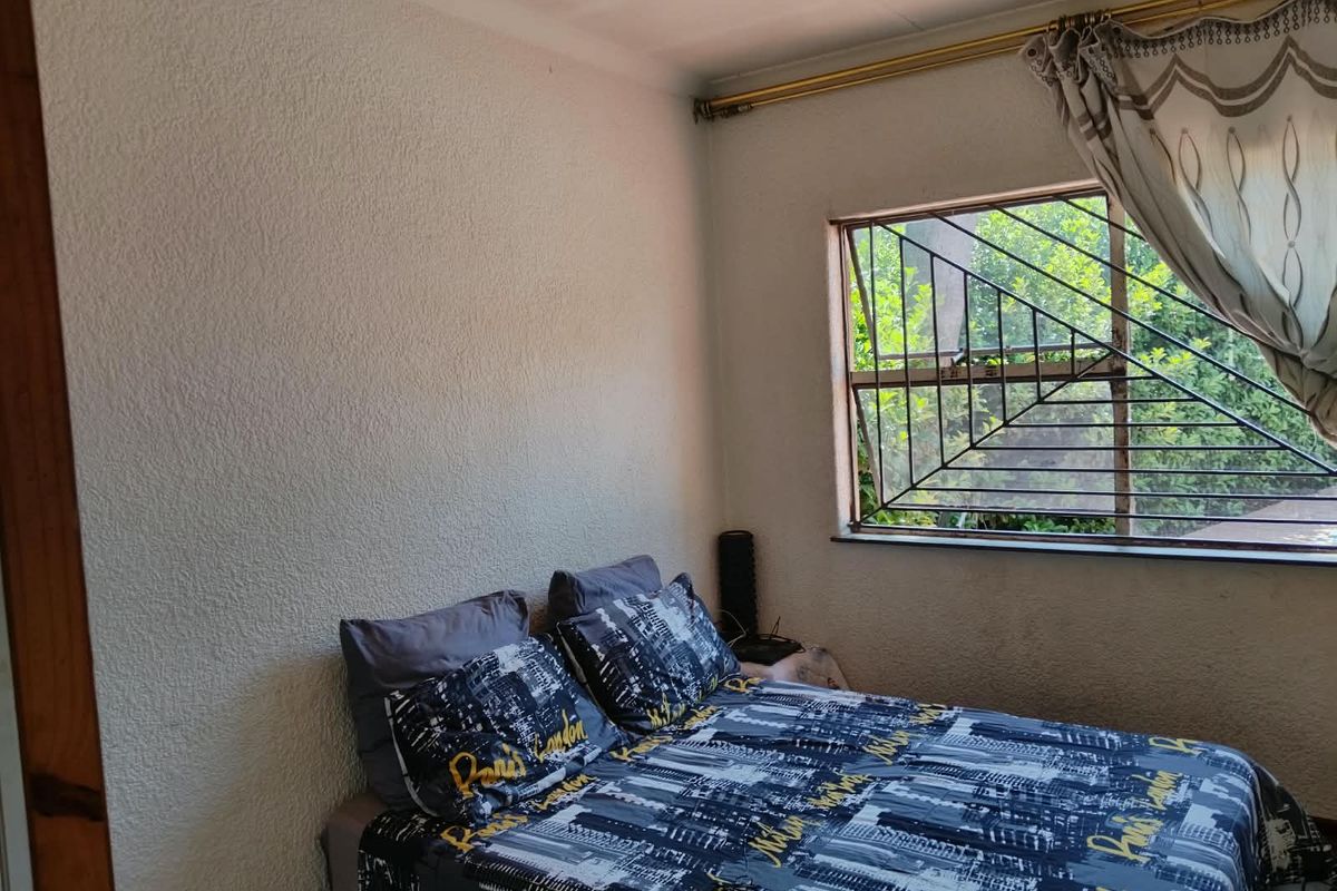 A bedroom featuring textured walls and a window fitted with security bars, offering a functional space with potential for cosmetic updates.