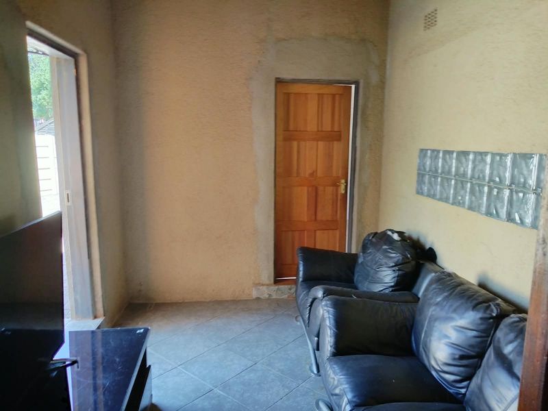 A living room space featuring tiled flooring, a glass block feature wall, and an unfinished doorway area requiring plastering and finishing.