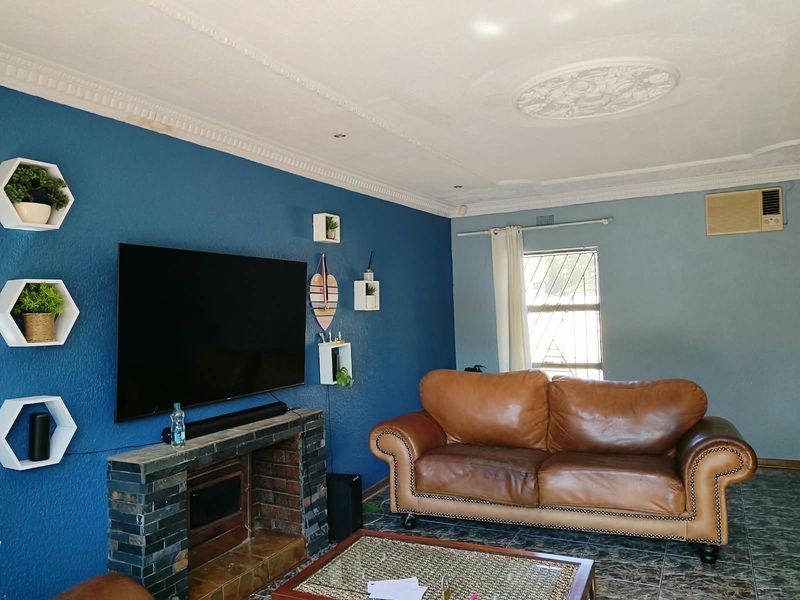 A living room featuring a brick fireplace, decorative ceiling rose, cornice detailing, and tiled flooring, with a wall-mounted air conditioning unit.