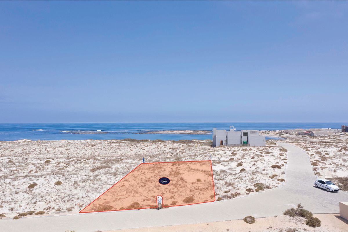 An aerial view of a vacant residential plot located in a coastal area, featuring direct road access and proximity to the ocean.