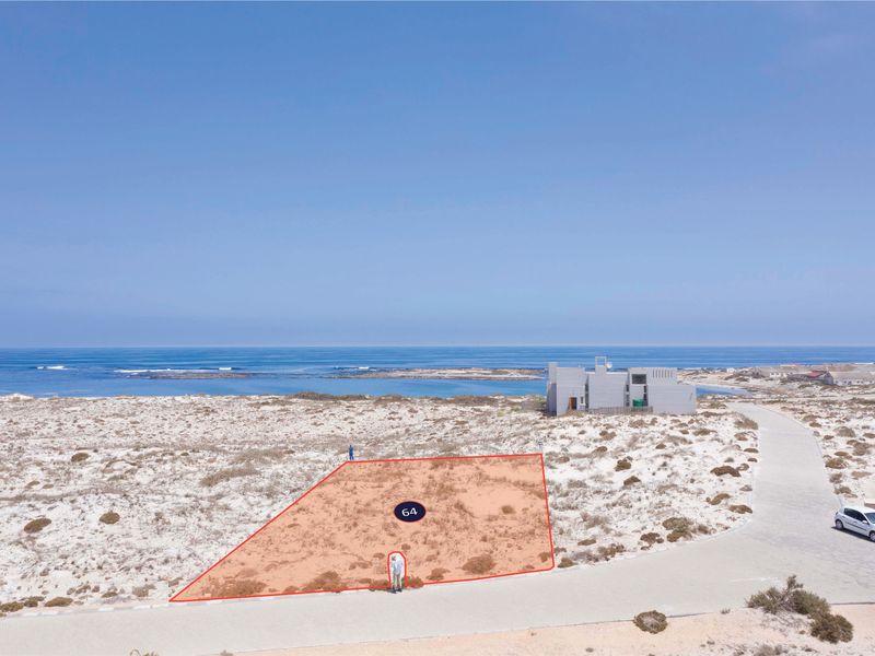An aerial view of a vacant residential plot located in a coastal area, featuring direct road access and proximity to the ocean.