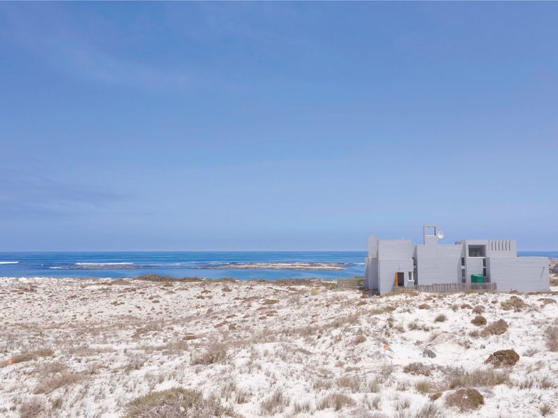 An aerial view of a coastal residential property situated amongst sand dunes with direct ocean views.