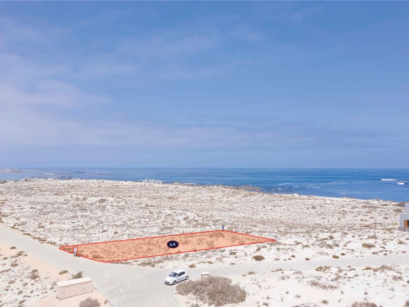 Aerial view of a vacant residential plot located in a coastal estate, featuring direct road access and proximity to the ocean.
