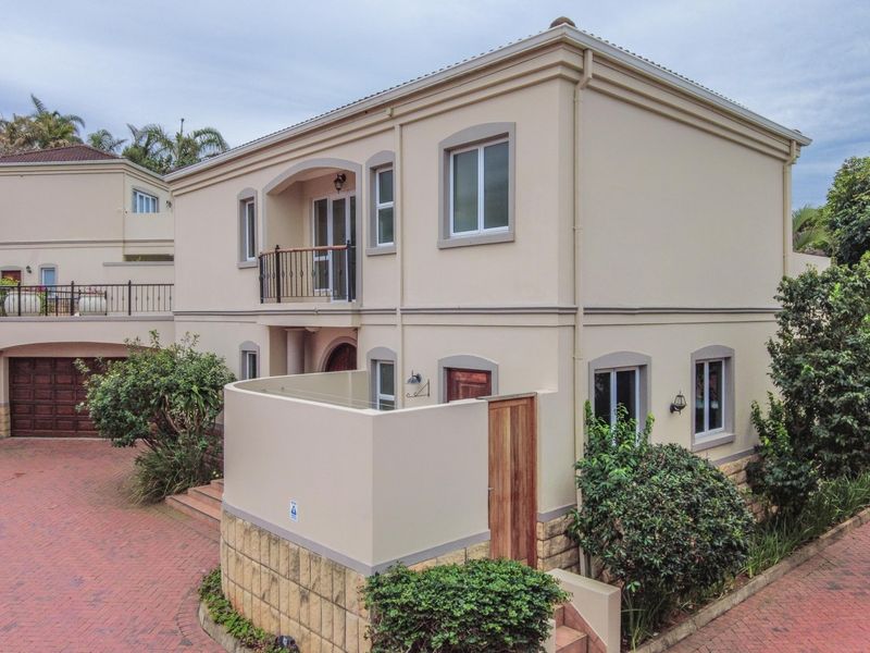 A well-maintained double-storey townhouse featuring a brick-paved driveway, a private balcony, and a double garage with stone-clad architectural detailing.