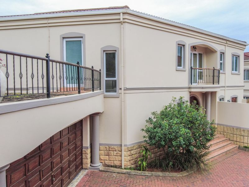 Front elevation of a townhouse featuring a raised terrace with wrought iron balustrade, stone cladding accents, and a paved driveway leading to the garage.