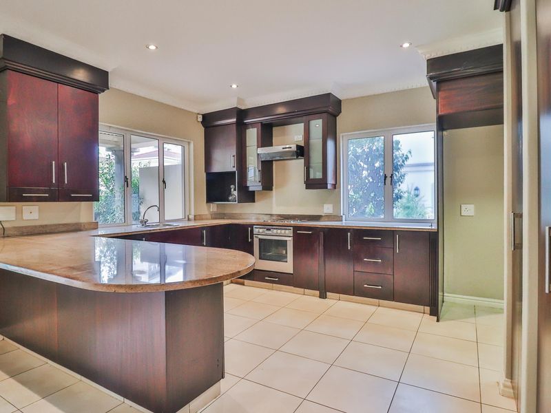 Spacious kitchen featuring dark wood cabinetry, granite countertops, built-in oven, gas hob, and tiled flooring with ample natural light.