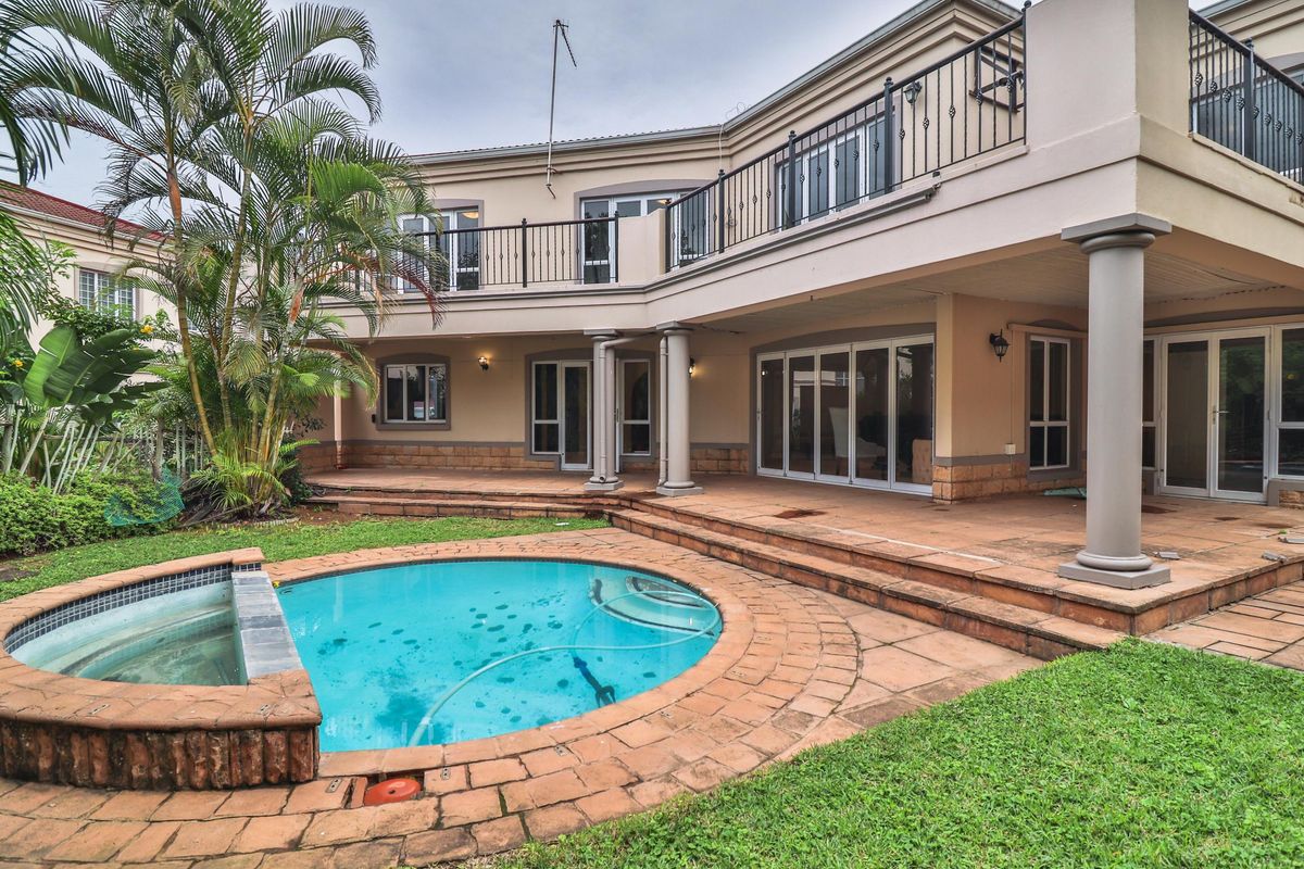 Rear view of the townhouse featuring a covered patio, upper balcony with wrought iron railings, and a private swimming pool set in a garden.
