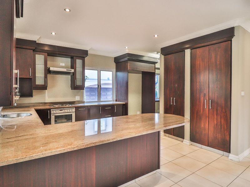 Spacious kitchen featuring dark wood cabinetry, granite countertops, built-in oven, hob, extractor fan, and tiled flooring.
