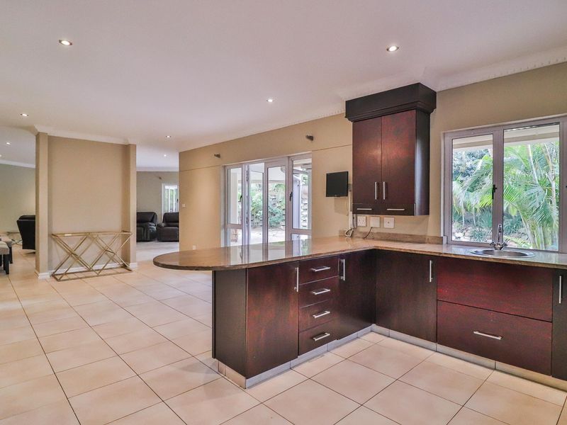 Open-plan kitchen featuring dark wood cabinetry, granite countertops, and tiled flooring, seamlessly flowing into the adjacent living area with access to the garden.