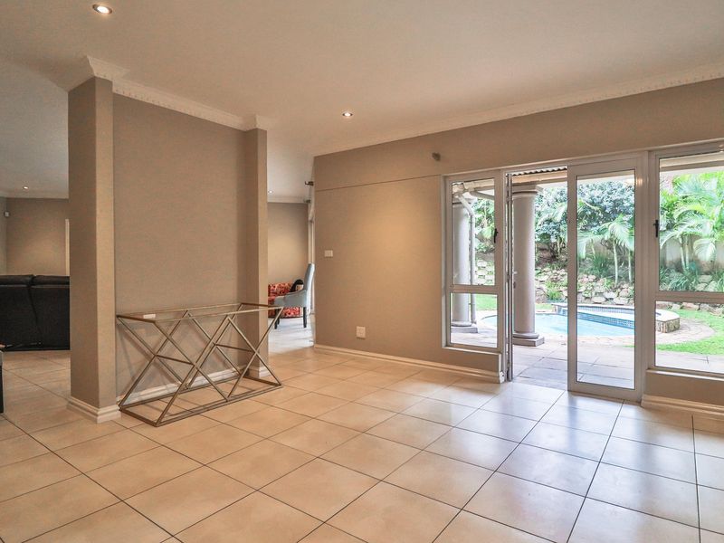 Spacious living area featuring neutral tiled flooring, recessed lighting, and large sliding glass doors providing direct access to the outdoor patio and pool area.