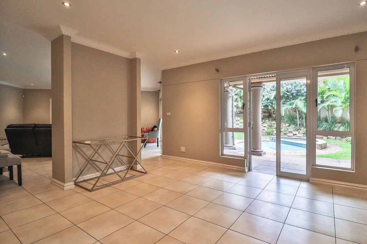 Spacious living area featuring neutral tiled flooring, recessed lighting, and large sliding glass doors providing direct access to the outdoor patio and pool area.