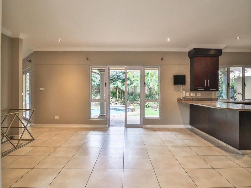 Spacious open-plan living area featuring tiled floors, recessed lighting, and a modern kitchen with granite countertops, flowing directly to the outdoor pool area.