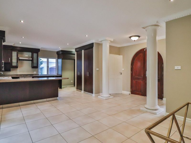 Spacious open-plan living area featuring dark wood cabinetry, stone countertops, decorative columns, and tiled flooring, creating a versatile and well-lit interior space.