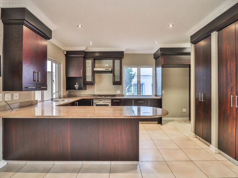 Spacious kitchen featuring dark wood cabinetry, granite countertops, built-in oven, gas hob, and tiled flooring with recessed lighting.