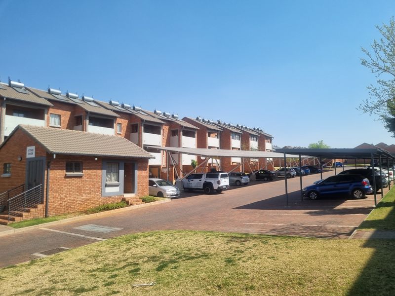 Exterior view of a multi-story apartment complex featuring brick construction, tiled roofing with solar geysers, and covered parking bays.