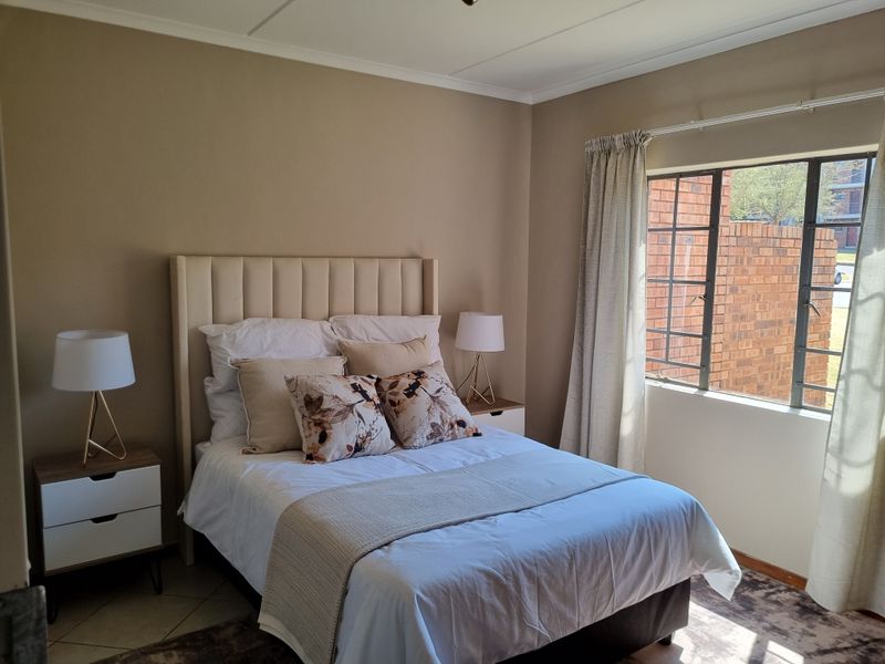 A well-maintained bedroom featuring neutral wall tones, tiled flooring, and a large steel-framed window allowing for natural light.
