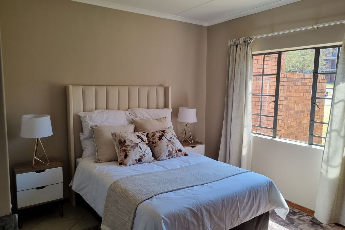A well-maintained bedroom featuring neutral wall tones, tiled flooring, and a large steel-framed window allowing for natural light.