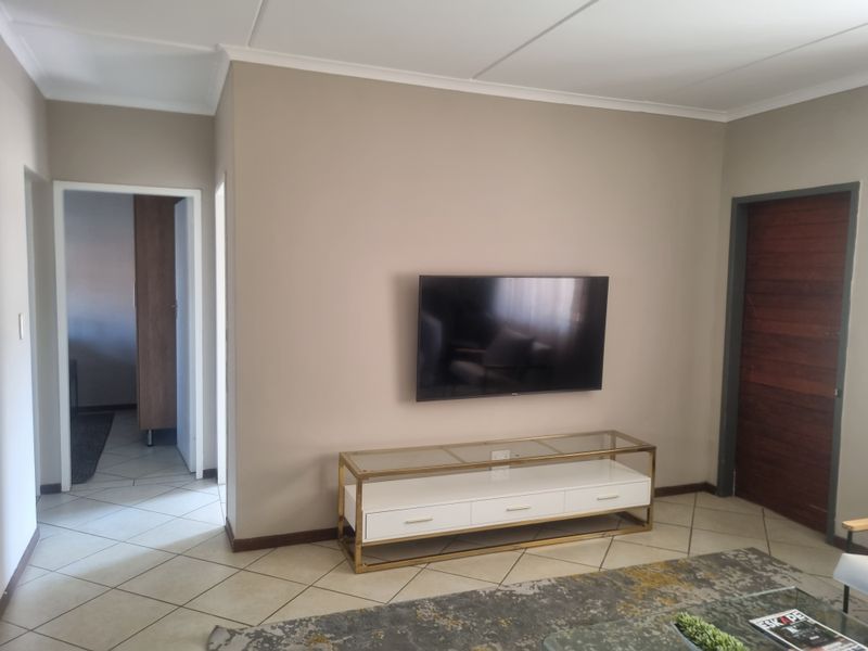 A well-maintained living room featuring neutral wall tones, tiled flooring, and a solid timber door leading to adjacent living spaces.