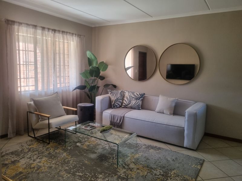 A comfortable living room featuring tiled flooring, neutral wall tones, and natural light filtering through window treatments.
