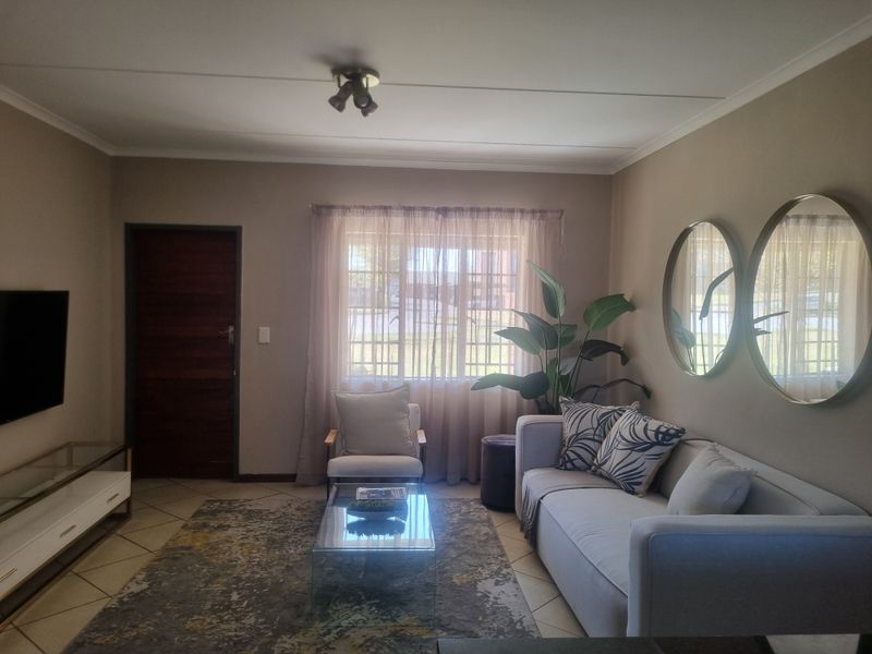 A well-maintained living room featuring tiled flooring, neutral wall tones, and natural light through a window with curtain treatments.