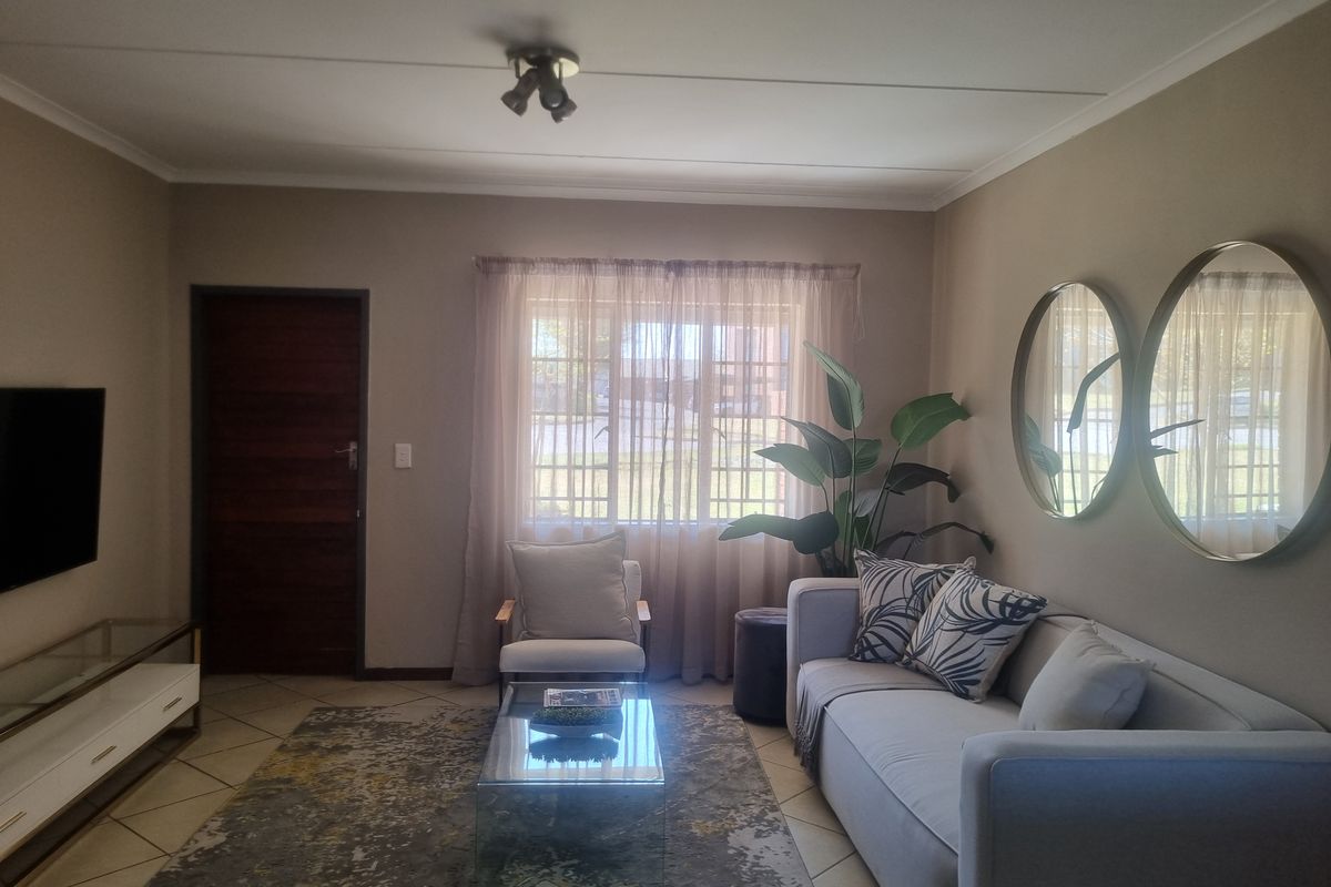 A well-maintained living room featuring tiled flooring, neutral wall tones, and natural light through a window with curtain treatments.