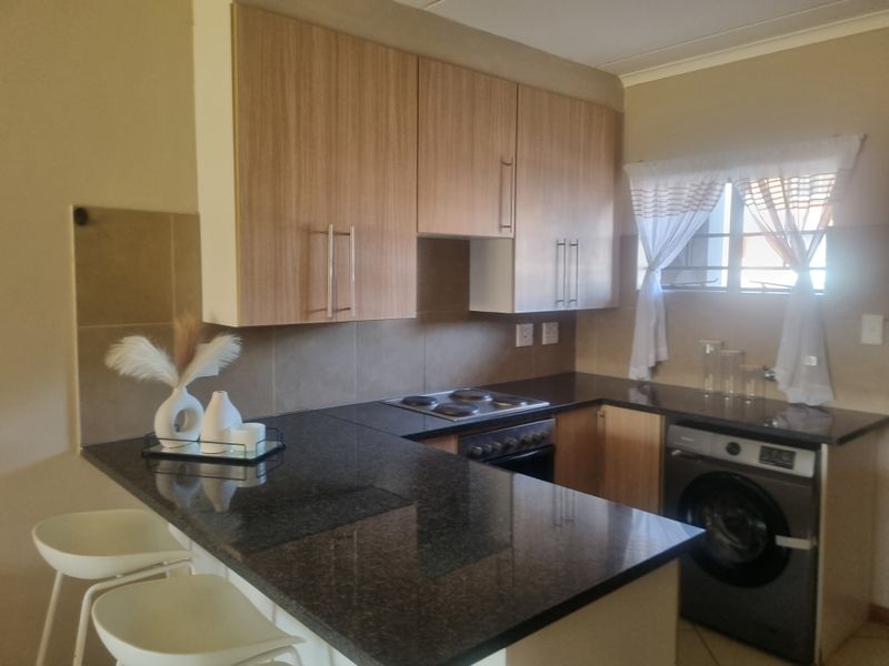 A functional kitchen featuring granite countertops, wood-finish cabinetry, a built-in electric hob and oven, and space for a washing machine.
