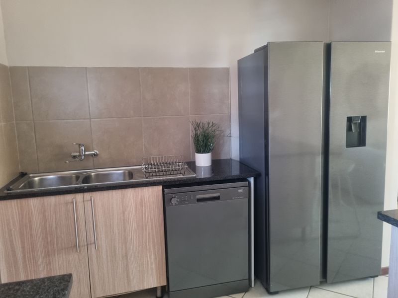 A functional kitchen area featuring laminate cabinetry, granite countertops, a double sink with tiled backsplash, and space for a large refrigerator and dishwasher.
