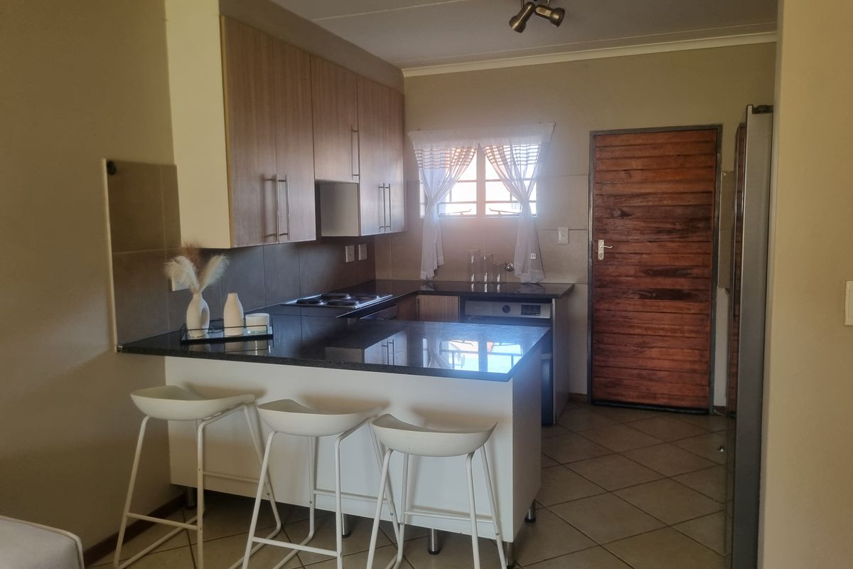 A functional kitchen featuring built-in cabinetry, granite countertops, an electric hob, and tiled flooring, with direct access to an exterior timber door.