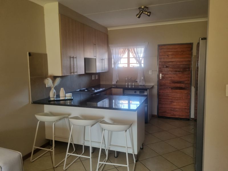 A functional kitchen featuring built-in cabinetry, granite countertops, an electric hob, and tiled flooring, with direct access to an exterior timber door.